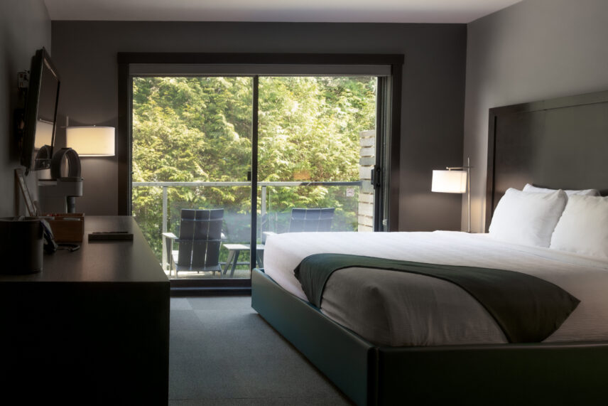 Morning light streaming through trees into a king room with soft textures and balcony access