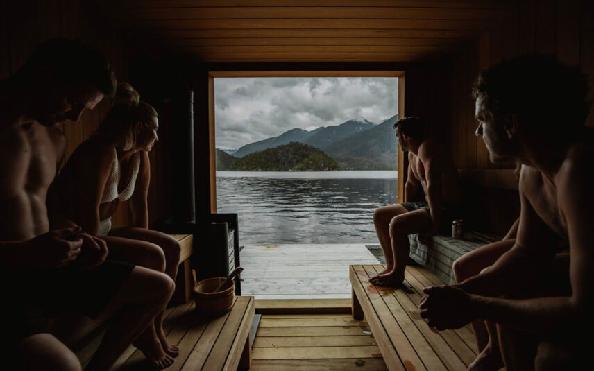Guests relaxing inside the floating sauna with panoramic views of the Tofino inlet and surrounding mountains