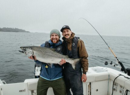 Two men holding a big fish smiling on a boat with fishing rod in background