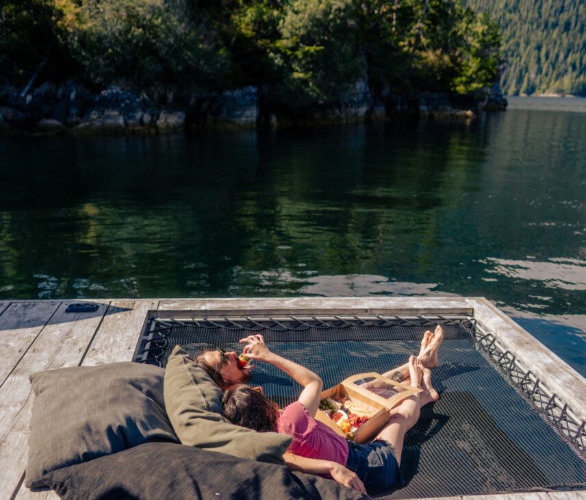 A couple in a hammock eating food at the Remote Floating Sauna